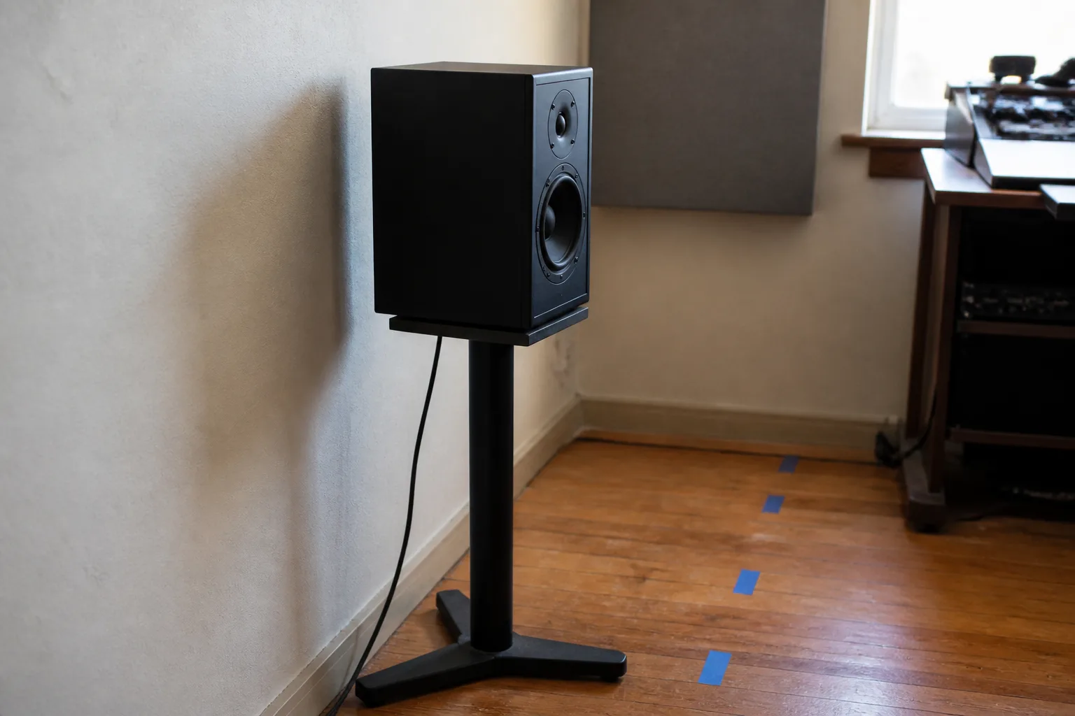 A studio monitor positioned near a wall with several floor markers for testing different distances.